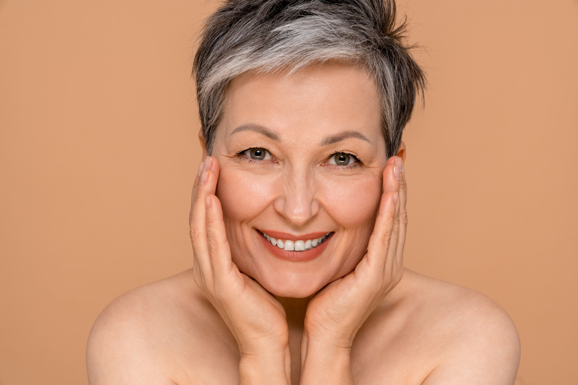 Mujer de cabello canoso sonriendo con las manos en el rostro